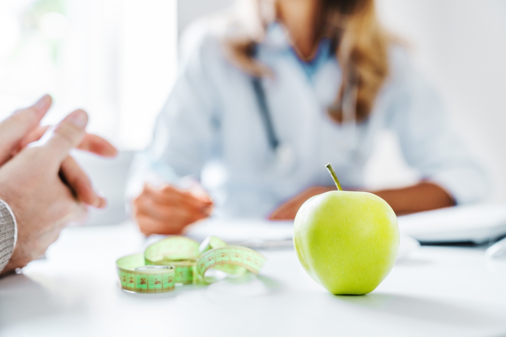 Cropped close up of woman doctor dietician recommending senior male patient fresh apple.