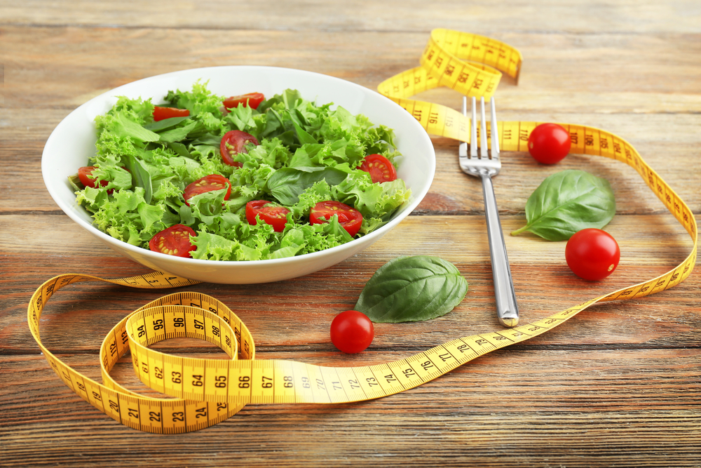 Fresh salad and measuring tape on wooden background.